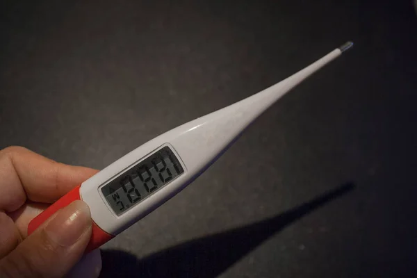 person holding a digital thermometer on black background