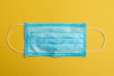 Sarı arka planda mavi tıbbi maske. Koronavirüs. Grip virüsü, soğuk algınlığı. Bakterilere karşı koruma. mesaj için yer. Salgın. Salgın. COVID-19, NCoV, 