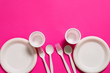 Tek kullanımlık iki kaşık, çatal, tabak ve pembe arka planda bir bardak mısır nişastası. Biyo-çözünebilir yemekler. Çevre dostu tecrit. Plastiğin modern biyomateryallerle değiştirilmesi
