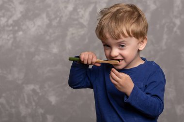 Küçük çocuk, dişlerini bir bambu diş fırçasıyla banyoda gri dokuda fırçalıyor. yatay fotoğraf. Çevre dostu. Sabah hijyeni konsepti. metin için yer.