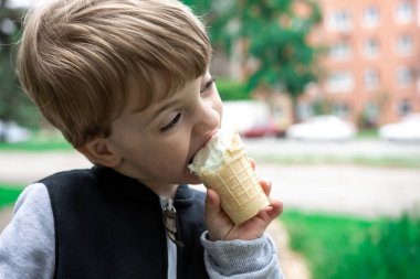 Küçük çocuk parkta doğanın arka planında bir dilim dondurmayı ısırıyor. Yaz gününde nefis bir tatlı. yakın plan portre