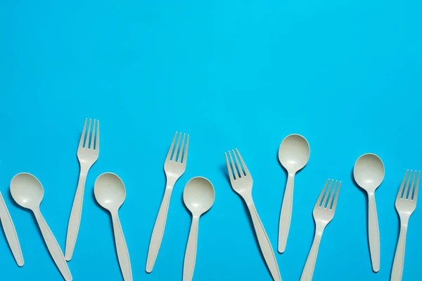 biodegradable disposable forks and spoons of corn starch on a blue background. eco friendly concept. place for text. picnic dishes made of modern materials instead of plastic.
