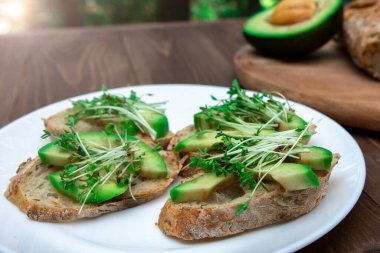 Pencere zemininde beyaz bir tabakta avokado ve kressalate mikroyeşili sandviçler. Sağlıklı beslenme. Besleme seçeneği. vejetaryenlik.