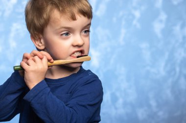 Üç yaşındaki bir çocuk banyoda dişlerini bambu bir diş fırçasıyla mavi dokuda fırçalıyor. yatay fotoğraf. Çevre dostu. Sabah hijyen konsepti.