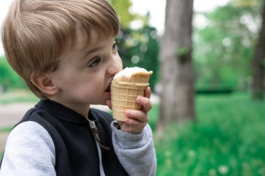 Küçük çocuk parkta doğanın arka planında bir dilim dondurmayı ısırıyor. Yaz gününde nefis bir tatlı. yakın plan portre