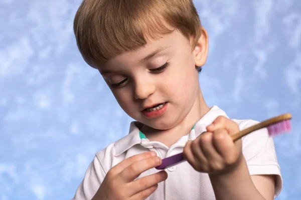 a three year old boy holds a bamboo toothbrush in his hand and examines it. eco friendly. replacing plastic with biodegradable hygiene items. European facial features.