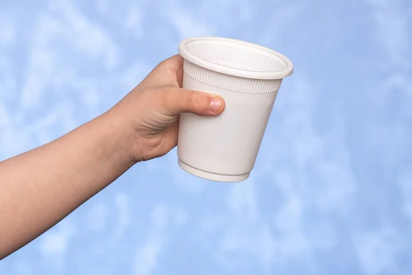 biodegradable disposable cup in a male hand. corn starch dishes. Replacing plastic with environmentally friendly materials. blue background.