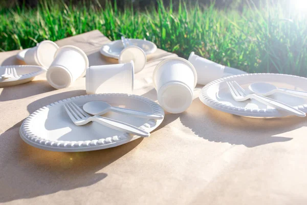 biodegradable disposable tableware from environmentally friendly materials. spoons, forks, glasses and plates of corn starch in nature on kraft paper. shadow from the grass. close-up. sun flare