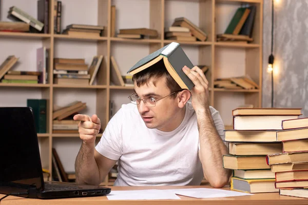 young man sits at a table with books and shows a finger to a laptop. remote work. difficulties of online learning. businessman manages staff from home.