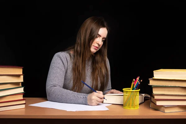 若い女子学生は黒い壁の背景に本が書かれた机に座っています ビジネス レディーは書類に 隔離における電気通信及び学習の難しさ — ストック写真