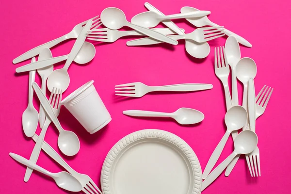 organic disposable cornstarch forks, spoons, plate and glasses on pink background. isolate. eco friendly. modern replacement of plastic dishes with biodegradable materials.