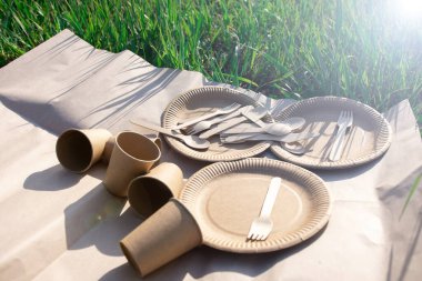 sets of disposable biodegradable tableware on kraft paper in nature. biodegradable plates and glasses of paper and spoons, forks and knives made of wood. environmentally friendly modern plastic replac clipart