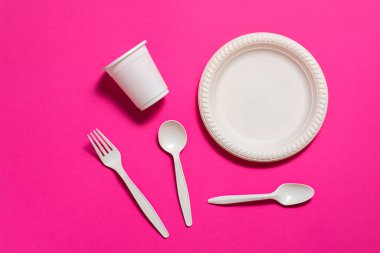 Tek kullanımlık organik mısır nişastası çatalları, kaşıklar, tabaklar ve pembe arka planda bardaklar. İzole et. Ekolojik olarak temiz. Plastik tabakların yerini biyolojik olarak bozunabilir malzemeler aldı..