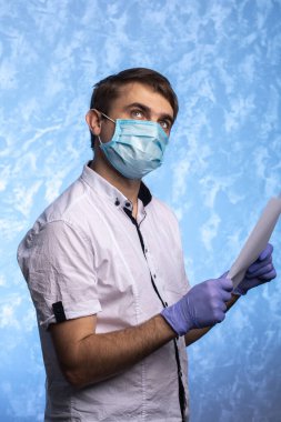 Tıbbi maskeli ve eldivenli genç adam bir belge okuyor. Doktor karantina sırasında güvenlik önlemlerine dikkat eder. bireysel koruma.