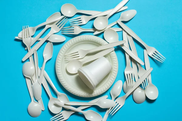 Tek kullanımlık sofra takımı: çatallar, kaşıklar, tabaklar ve mavi arkaplanda mısır nişastasından yapılmış bardaklar. İzole et. Çevre dostu. Plastik tabakların yerini biyolojik olarak ayrıştırılabilir organik malzemeler aldı..