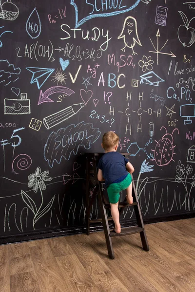 a little boy climbs the stairs near a large slate wall with multi-colored chalk drawings.