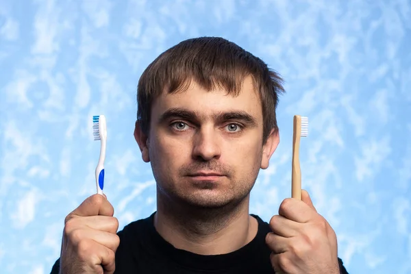 Молодой Человек Держит Руках Пластиковые Бамбуковые Зубные Щетки Задумчивый Взгляд — стоковое фото
