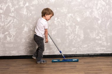 Üç yaşındaki bir çocuk dairede yerleri yıkıyor. Tüm aileyle birlikte evin genel temizliği. Küçük bir çocuk ebeveynlere yardım eder. arkaplanda gri duvar.