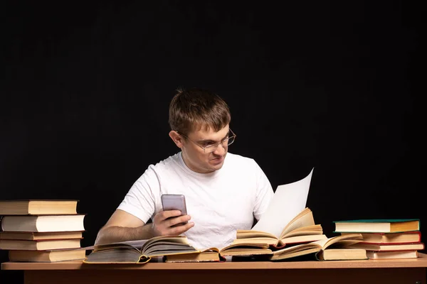 Joven Estudiante Sienta Una Mesa Con Libros Sobre Fondo Negro —  Fotos de Stock