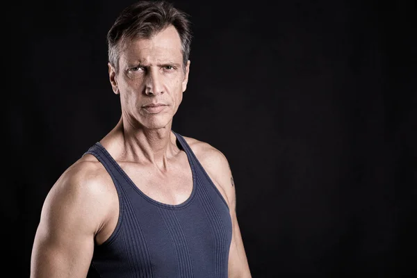 40-50 yaşlarında, yeleği olan, kameraya bakan zinde bir adam.