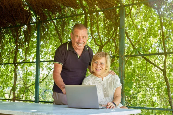 Smiling senior couple surfing online with a computer in natural and green location - Concept of active elderly and interaction with new technologies