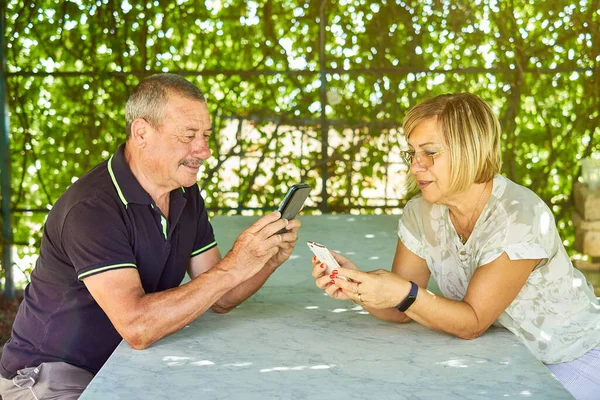 Portrait of positive mature couple chatting using phone into a natural and green location Royalty Free Stock Images
