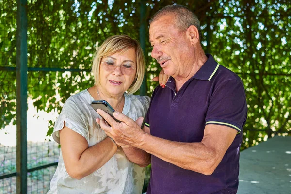 Senior couple using a mobile phone for finding some online in a natural and green location - Concept of active elderly and interaction with new technologies Royalty Free Stock Images