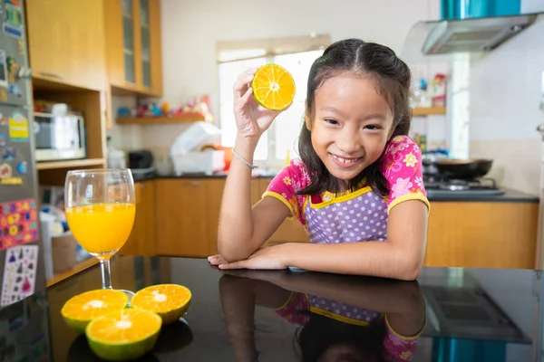 小亚洲女孩在厨房喝橙汁 — 图库照片