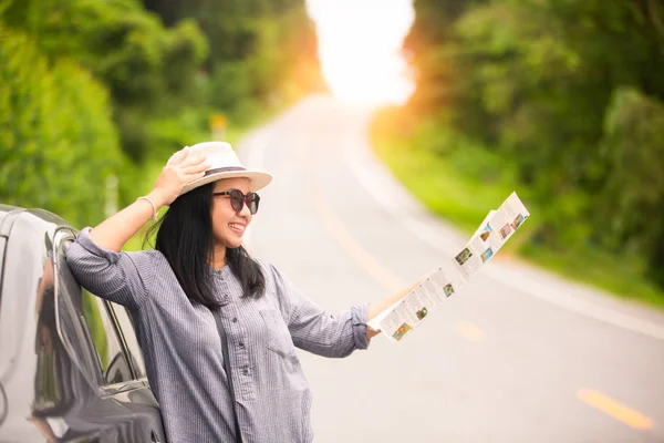 Asian traveler woman using map beside car at hill road . Travel concept