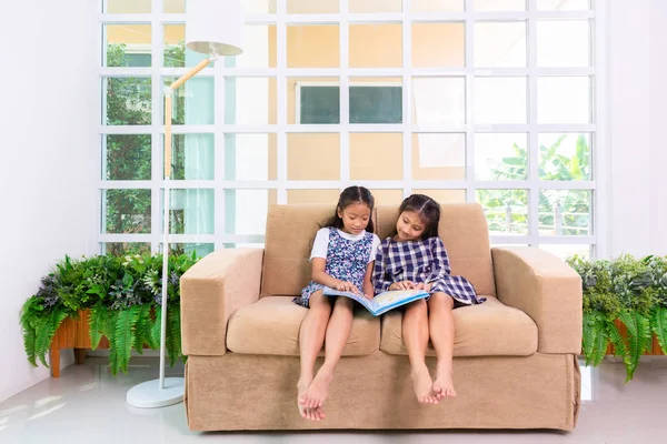 Små elev tjejer tycker om att läsa bok om soffan hemma — Stockfoto