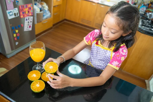 Kleine asiatische Mädchen trinken Orangensaft in Küche — Stockfoto