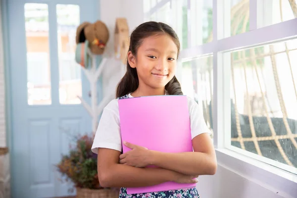 छोटी एशियाई लड़की मुस्कुरा रही और घर पर किताबें पकड़ रही है — स्टॉक फ़ोटो, इमेज