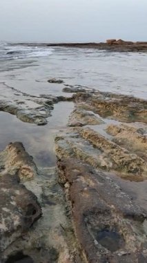 Sahilden gün batımı. Kayalık arazi ve bulutlu ufuk.