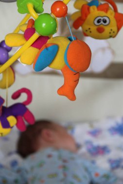 Yatakta uyuyan bir bebeğin arka planında parlak bir oyuncağın fotoğrafı. Bebek fotoğrafçılığı, bebek beşiği oyuncağı. Çocuk odasında kullanılabilir..