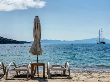 Güneş yatakları ve arka planda deniz ve dağlara karşı bir şemsiye. Eğlence ve turizm konsepti.