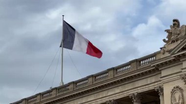Bir video, Fransa bayrağının rüzgarda yavaşça dalgalandığını gösteriyor. Görkemli, klasik bir binanın tepesinde. Bayrak dramatik bir şekilde dalgalanırken mavi, beyaz ve kırmızı dikey çizgiler açıkça görülebilir.