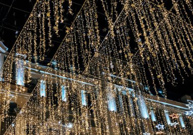 Binlerce pırıl pırıl altın ve mavi peri ışığıyla kaplı sokak ya da halka açık bir tavan arasında büyüleyici bir gece görüntüsü. Işıkların telleri bir perde gibi sarkıyor ve büyülü bir şey yaratıyor.