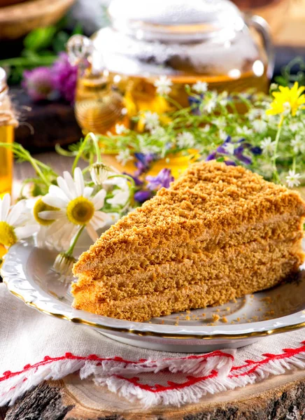piece of honey cake  close-up on white plate, linen cloth and wooden slice decorated with wild flowers in rustic style