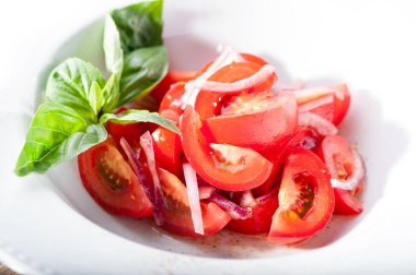 domates salatası, fesleğen yaprakları ve baharatlar beyaz plaka yakın çekim ile kırmızı soğan 