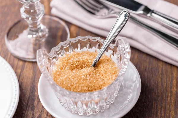 crystal bowl with brown sugar,  spoon and white saucer close-up on table served with cutlery