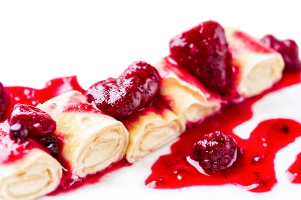 curd cream rolled pancakes close-up with berry syrup,   strawberries and blackberries on white background