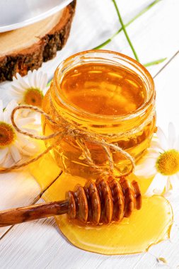 beyaz ahşap arka plan üzerinde ip, dipper ve papatya çiçekleri yakın çekim ile süslenmiş bal küçük cam kavanoz  