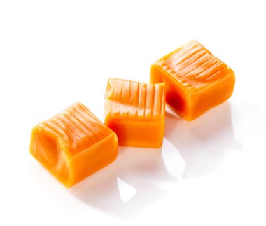 Sıraya dizilmiş üç karamel şeker beyaz arka planda izole edilmiş, gölgeli. 