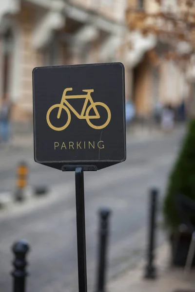 Parking sign for bicycles. The sign shows a bicycle and the inscription parking. In the background is a paved road and a house.