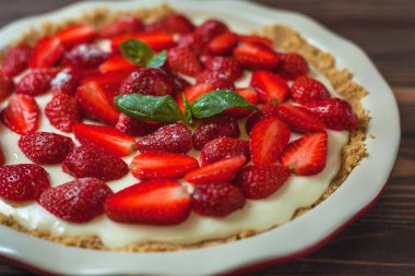 Fesleğen yapraklı çilekli cheesecake, ahşap arka planda kırmızı seramik bir fırın kabında. Seçici odak