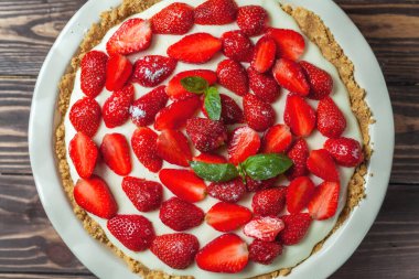 Fesleğen yapraklı çilekli cheesecake, ahşap arka planda kırmızı seramik bir fırın kabında.