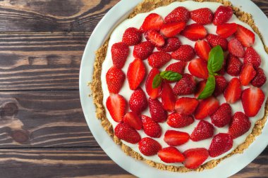 Fesleğen yapraklı çilekli cheesecake, ahşap arka planda kırmızı seramik bir fırın kabında.