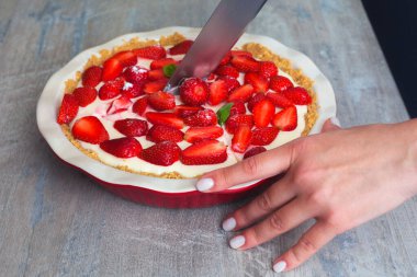 Kırmızı seramik fırın kabında fesleğen yapraklı çilekli cheesecake. Kız turtayı keser. ahşap arkaplanda