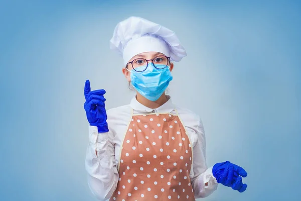 Girl cook wears a protective medical mask and rubber gloves. Virus protection and kitchen safety, pandemic concept. Isolated on blue background. Hight quality photo