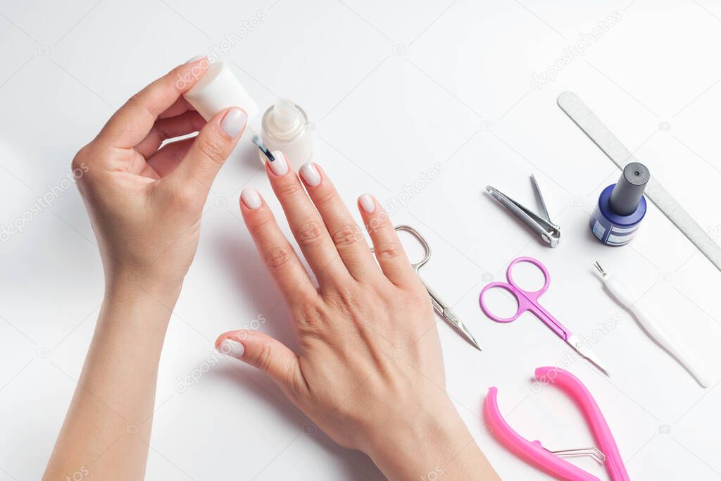 Female hands paint nails, next to lay down devices for nail care. The girl does a manicure. on white background. View from above. High quality photo